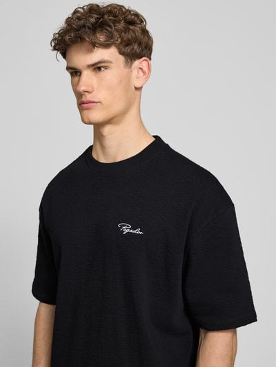 Männermodel trägt Oversized Herren T-Shirt aus reiner Baumwolle von Pegador, Modell 'Signar' mit Logo-Stitching, 1/2-Arm, Nahaufnahme Oberkörper.