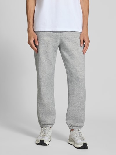 Männermodel trägt Sweatpants mit Label-Detail von Champion in Hellgrau, gerader Schnitt, Baumwollmischung, Ganzkörperansicht von vorne.