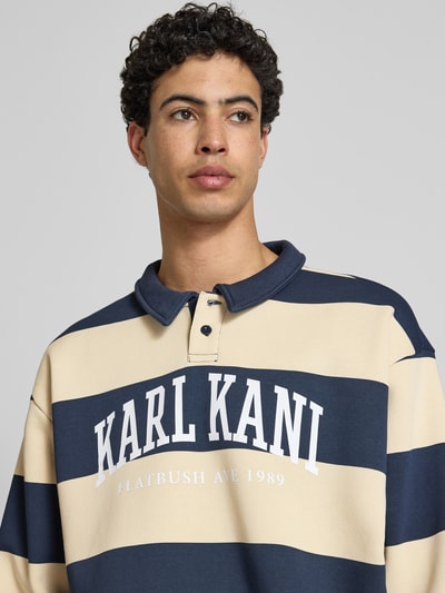 Männermodel trägt Oversized Sweatshirt mit Polokragen Modell 'Heritage' von KARL KANI im Baumwoll-Mix, Logo-Print, Nahaufnahme Oberkörper.