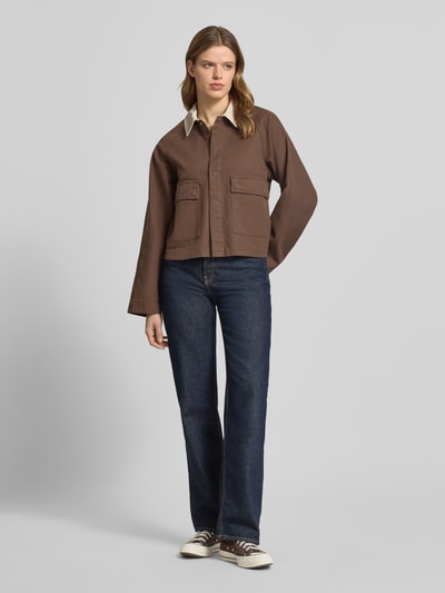 Modelka nosi Regular Fit Jeansjacke aus reiner Baumwolle Modell 'BETT' von Pieces, jednokolorowy brąz, obszycie ze sztruksu, denim, kieszenie z patką, krój regular fit, widok całej sylwetki z przodu.