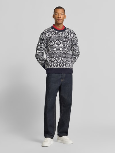 Męskia model nosi sweter 'Pullover mit Logo-Detail' od Tommy Hilfiger, wzór na całej powierzchni, imitacja dzianiny, aplikacja: detal z logo, kształt kołnierza: crew neck, okrągły dekolt, rękawy: długi rękaw, zakończenie rękawów: prążkowane, wykończenie: prążkowane, widok całej sylwetki z przodu.