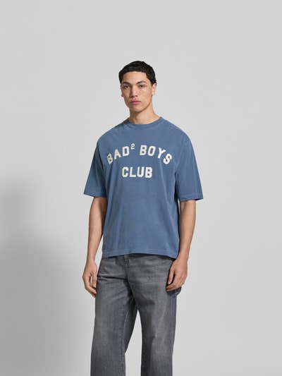 Männermodel trägt Loose Fit T-Shirt mit Rundhalsausschnitt von Dsquared2 in Blau mit Statement-Print und Used-Look, Ganzkörperansicht von vorne.