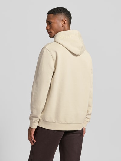 Männermodel trägt Regular Fit Hoodie aus reiner Baumwolle von Marc O'Polo in Beige, unifarben, Kapuze mit Label-Schriftzug, Ganzkörperansicht Rückansicht.