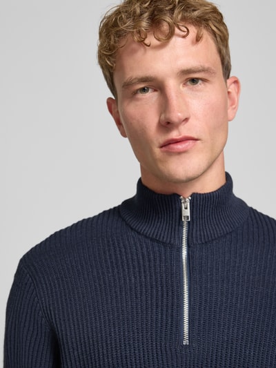 Męski model nosi sweter z dzianiny z mieszanki materiałów z bawełną, krój slim fit, model 'PANNEL' od JACK & JONES, kołnierz zapinany, zbliżenie górnej części ciała.