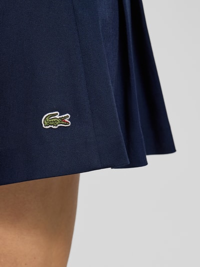 Frauenmodel trägt Mini-Rock aus Baumwoll-Mix von Lacoste Sport, unifarben dunkelblau, ausgestellte Form, Logo-Stitching, Detailaufnahme.
