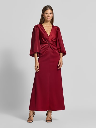 Frauenmodel trägt Cocktailkleid mit Knotendetail und V-Ausschnitt Modell 'THEA' von YAS in Rot, Material-Mix mit Stretch, Ganzkörperansicht von vorne.