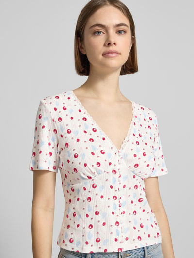 Frauenmodel trägt Blusenshirt in Pointelle-Optik Modell 'Vianne' von OH APRIL aus Reine Baumwolle, Weiß mit rotem Muster, Nahaufnahme Oberkörper.