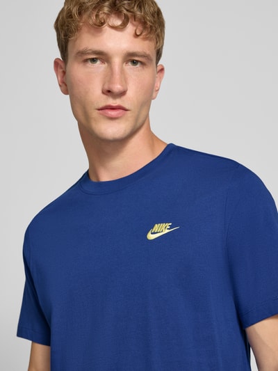 Männermodel trägt Regular Fit T-Shirt aus reiner Baumwolle von Nike in kräftigem Blau mit gelbem Logo, Nahaufnahme Oberkörper.