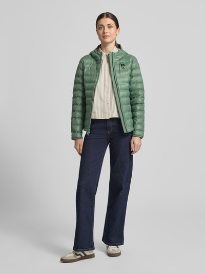 Frauenmodel trägt smaragdgrüne Steppjacke mit Kapuze, Zweiwege-Reißverschluss, Modell 'ELLIS' von Blauer Usa, Slim Fit, Ganzkörperansicht von vorne, Rückenlänge bei Größe S 57 cm, Schulterbreite 35 cm, Brustweite 48 cm, Ärmellänge 60 cm.