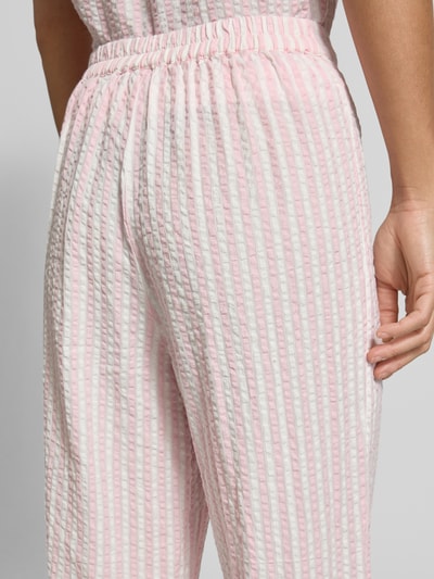 Frauenmodel trägt Straight Leg Hose aus reiner Baumwolle Modell 'TINNA' von Pieces mit rosa-weißem Allover-Muster, Crinkle-Struktur, Nahaufnahme Rückansicht.