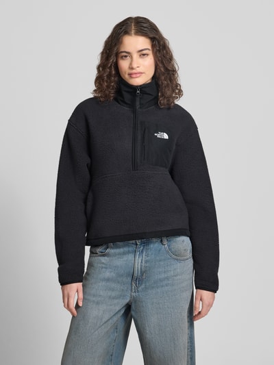 Frauenmodel trägt Fleecepullover mit Troyer-Kragen Modell 'YUMIORI' von The North Face in Schwarz, elastische Abschlüsse, Label-Detail, gerade Passform, Brustweite 56 cm, Rückenlänge 54 cm, Schulterbreite 51 cm, Ärmellänge 58 cm, Ganzkörperansicht von vorne.