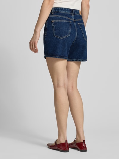 Frauenmodel trägt Bermuda Leg Jeansshorts aus reiner Baumwolle von Marc O'Polo Denim in dunklem Denim, 5-Pocket-Design, Twillstruktur, Ganzkörperansicht Rückansicht.