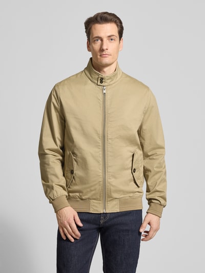 Mężczyzna nosi Jacke mit Stehkragen und Pattentaschen od Christian Berg Men, mieszanka bawełny i elastanu, krój regular fit, stójka, zamek błyskawiczny, kieszenie z patką, długość tyłu w rozmiarze M 32 cm, szerokość ramion w rozmiarze M 41 cm, szerokość w rozmiarze M 55 cm, długość rękawów w rozmiarze M 67 cm, jasnobeżowy, proste linie, lekko matowa tekstura, całkowity widok z przodu.