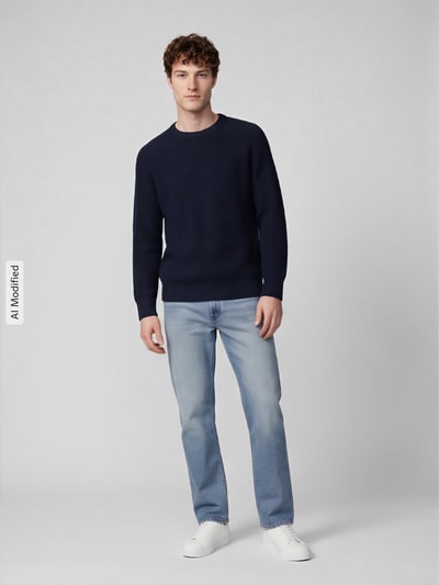 Männermodel trägt Regular Fit Pullover aus reiner Baumwolle Modell 'BRAUN' von Selected, dunkelblau, kombiniert mit Jeans, Herren Pullover, Ganzkörperansicht von vorne, KI-modifiziertes Bild.