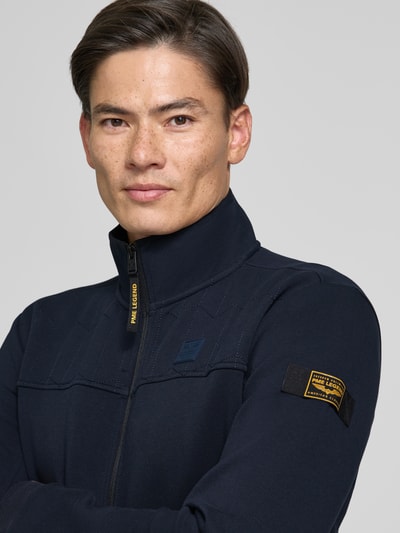 Männermodel trägt Sweatjacke mit Stehkragen und Label-Patch von PME Legend in Dunkelblau, Strukturmuster, Nahaufnahme Oberkörper.