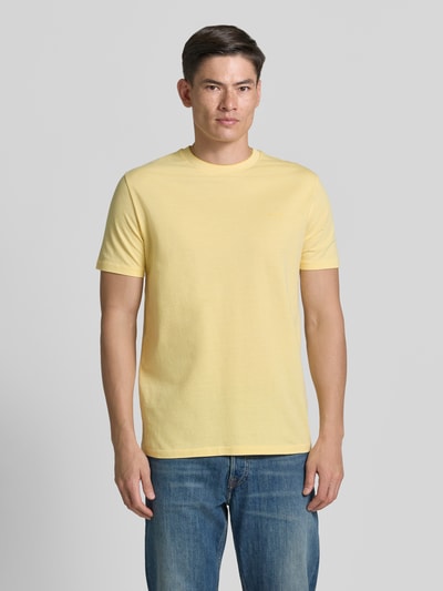 Männermodel trägt T-Shirt mit Rundhalsausschnitt und Label-Stitching von Gant in Gelb aus reiner Baumwolle, Regular Fit, Ganzkörperansicht von vorne.