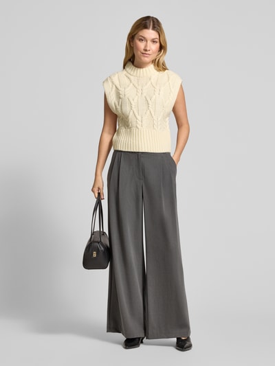 Frauenmodel trägt Strickpullunder aus Woll-Mix mit Stehkragen Modell 'MAGLE' von Cph Muse, cremefarben mit Zopfmuster, Regular Fit, kombiniert mit grauer weiter Hose, vielseitige Texturen und neutrale Töne, Ganzkörperansicht von vorne. Damen Strickpullunder, Rückenlänge bei Größe S: 50 cm.