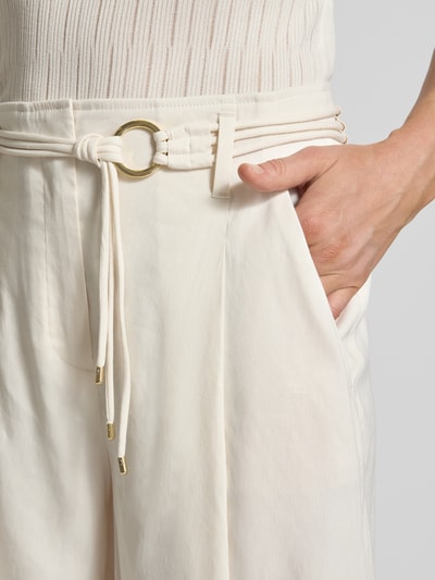 Vrouwenmodel draagt Wide Fit Shorts aus Leinen-Mix mit Viskose-Anteil van Marc Cain, lichte naturel kleur, bandplooien, steekzakken, binnenbeenlengte maat 36: 50 cm, mix van linnen en viscose, haakjes- en ritssluiting, detailopname taille en zak.