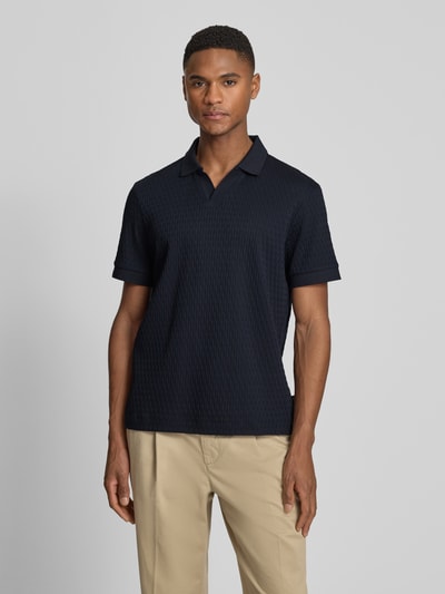 Męski model nosi Regular Fit Poloshirt mit V-Ausschnitt Modell 'Rauljose' von JOOP! Collection z bawełny, fakturowany wzór, krój regular fit, długość tyłu w rozmiarze M 69 cm, kolor ciemnogranatowy, widok całej sylwetki z przodu