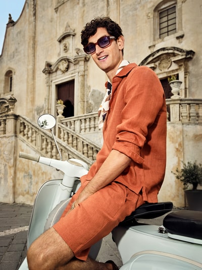 Männermodel trägt Bermudas aus reinem linnen von JAKE*S STUDIO MEN in oranje tint, met knoop- en ritssluiting, riemlussen, steekzakken, stolpplooi, bandwijdte maat M 45 cm, binnenbeenlengte 24 cm, los model, vooraanzicht bovenlichaam.