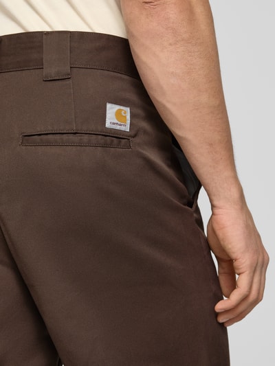 Männermodel trägt braune HOSE mit Gesäßtaschen Modell 'Denison' von Carhartt Work In Progress, Material-Mix, Nahaufnahme Rückansicht.