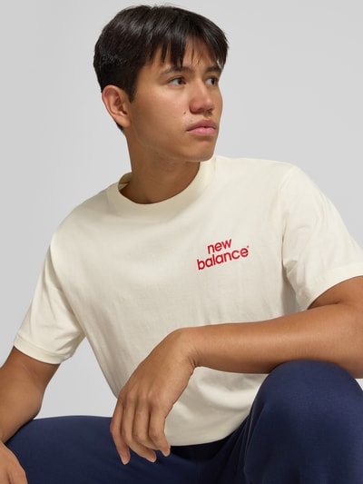 Männermodel trägt Regular Fit T-Shirt aus reiner Baumwolle Modell 'INTELLIGENT' von New Balance, naturweiße Farbe mit rotem Label-Detail, Kontext: Herren T-Shirt, rückseitiger Print, Rückenlänge Größe M 72 cm, Nahaufnahme Oberkörper.