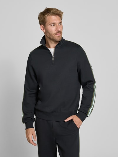 Männermodel trägt Sweatshirt aus Baumwoll-Mix von Paul Smith in Schwarz mit Troyer-Kragen, lockerer Passform und elastischen Abschlüssen, Ganzkörperansicht von vorne. Rückenlänge bei Größe M 68 cm, Ärmellänge 70 cm.