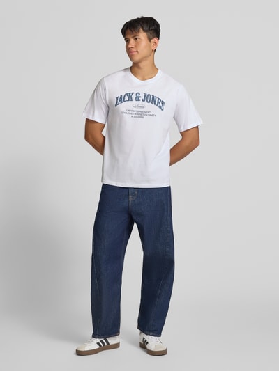 Männermodel trägt Regular Fit T-Shirt aus reiner Baumwolle Modell 'Denver' von JACK & JONES in Weiß mit blauem Logo-Print, Ganzkörperansicht von vorne. Rückenlänge bei Größe M: 69 cm.