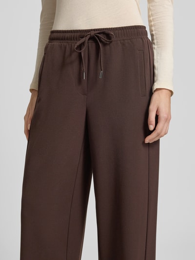 Kobiece modelka nosi Hose mit elastischem Bund Modell 'Melane flow' od OPUS, materiałowy miks z domieszką wiskozy, krój regular fit, szerokość w rozmiarze 36: 39 cm, długość wewnętrzna nogawki w rozmiarze 36: 81 cm, ciemny brąz, wizualna faktura gładka, zbliżenie na górną część spodni