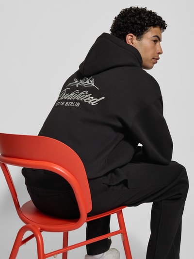 Männermodel trägt schwarzen Oversized Hoodie mit Label-Stitching von PROHIBITED aus Baumwoll-Mix, gerippte Abschlüsse, Rückenlänge 67 cm, Ärmellänge 59 cm, Kapuze und Känguru-Tasche, Ganzkörperansicht Rückansicht.