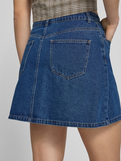 Frauenmodel trägt A-Linie Jeansrock aus Baumwoll-Mix mit Viskose-Anteil Modell 'ABBI' von Pieces, Denim-Optik, Twillstruktur, Ganzkörperansicht Rückansicht.