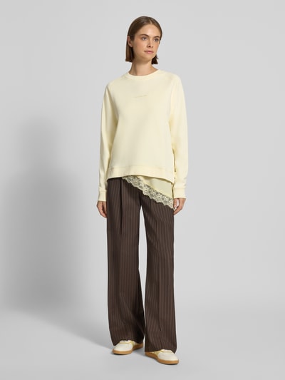 Frauenmodel trägt Regular Fit Sweatshirt aus reiner Baumwolle von Marc O'Polo DENIM in Gelb, kombiniert mit brauner Hose, Ganzkörperansicht von vorne.