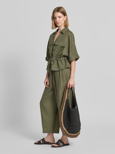 Frauenmodel trägt Relaxed Fit Leinenbluse mit Brusttaschen von Christian Berg Woman in Olivgrün, Hemdblusenkragen, V-Ausschnitt, Knopfleiste, Schnürung, reine Leinen-Textur, Ärmel mit Aufschlag, Ganzkörperansicht von vorne.