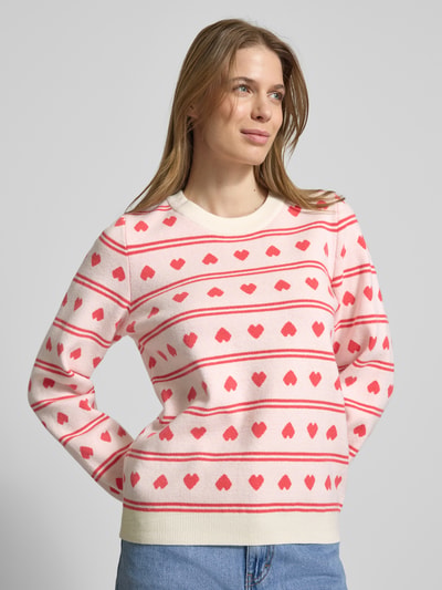 Frauenmodel trägt Relaxed Fit Pullover mit Allover-Motiv-Stitching Modell 'Brielle' von ICHI in Strick-Optik, Rosa mit roten Herzen, Rundhalsausschnitt, elastische Abschlüsse, Ganzkörperansicht von vorne.