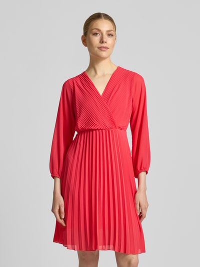 Frauenmodel trägt knielanges Kleid mit Plisseefalten Modell 'Im44sa' von ZABAIONE in Rot, taillierter Schnitt, Wickel-Optik, Ganzkörperansicht von vorne.