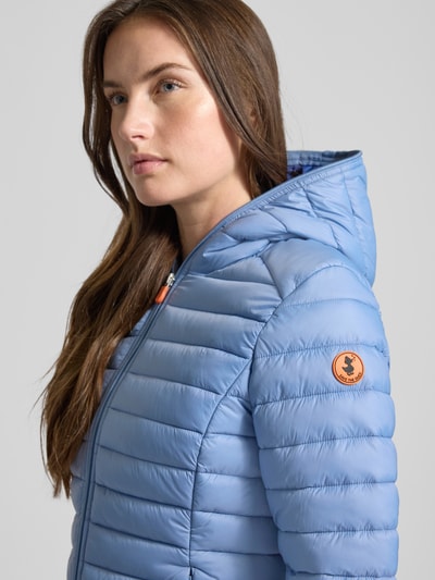 Frauenmodel trägt Slim Fit Steppjacke im Zweiwegereißverschluss Modell 'Daisy' von SAVE THE DUCK in Hellblau, Stepp-Optik, Nahaufnahme Oberkörper.