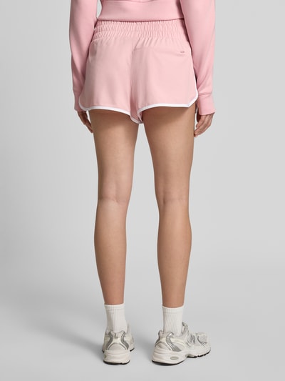 Frauenmodel trägt Running Shorts mit elastischem Bund von VARLEY in Rosa mit weißer Paspel, Material-Mix mit Stretch, Relaxed Fit, Ganzkörperansicht Rückansicht.
