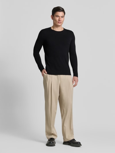 Männermodel trägt Slim Fit Pullover in Strick-Optik Modell 'Mino' von Drykorn aus Reine Baumwolle mit Rundhalsausschnitt, schwarze Farbe, Ganzkörperansicht von vorne.