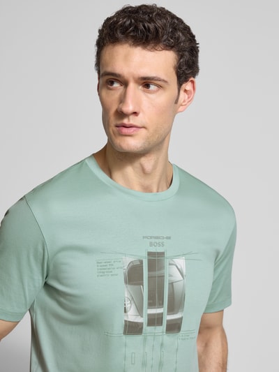 Männermodel trägt Regular Fit T-Shirt aus reiner Baumwolle Modell 'SPIRIT70' von BOSS Green x Porsche in Mintgrün mit Motiv-Print, Nahaufnahme Oberkörper.