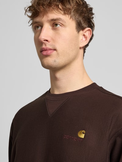 Männermodel trägt Sweatshirt mit Label-Stitching von Carhartt Work In Progress in Braun aus Baumwoll-Mix, Nahaufnahme Oberkörper.