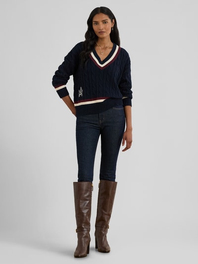 Frauenmodel trägt Regular Fit Strickpullover aus reiner Baumwolle von Lauren Ralph Lauren in Optik: Unifarben mit Zopfmuster, Logo-Detail, Label Stitching und Kontraststreifen, gerippte Abschlüsse, V-Ausschnitt, Langarm, Materialverarbeitung: Strick, Ganzkörperansicht von vorne.