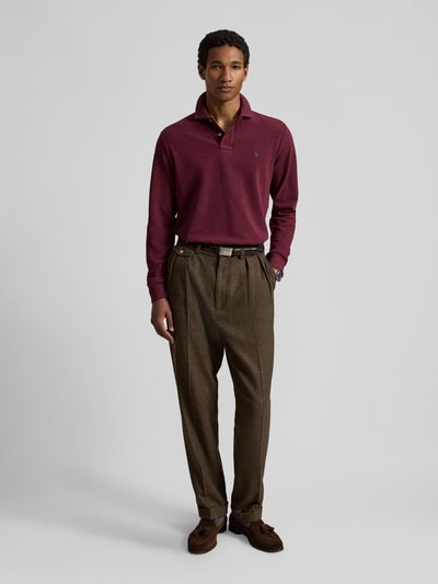 Männermodel trägt Regular Fit Poloshirt aus reiner Baumwolle von Polo Ralph Lauren in Weinrot, kombiniert mit brauner Hose, Ganzkörperansicht von vorne. Herren Poloshirt von Polo Ralph Lauren.