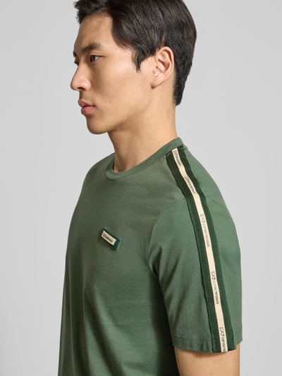 Męski model nosi Regular Fit T-Shirt mit Logo-Patch od EA7 Emporio Armani, czysta bawełna, okrągły dekolt, ujęcie z boku, zbliżenie na górną część ciała.