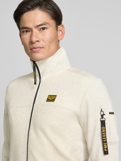 Männermodel trägt Sweatjacke mit Stehkragen und Label-Patch von PME Legend in Beige, Strukturmuster, Nahaufnahme Oberkörper. Material-Mix mit Baumwoll-Anteil, Reißverschluss mit Label-Detail, Reißverschlusstasche am Ärmel, seitliche Eingrifftaschen.