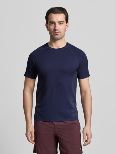 Męski model nosi Regular Fit T-Shirt mit Logo-Print von Fabletics w kolorze granatowym, okrągły dekolt, krótkie rękawy, długość tyłu w rozmiarze M: 67 cm, krój regular fit, widok całej sylwetki z przodu.
