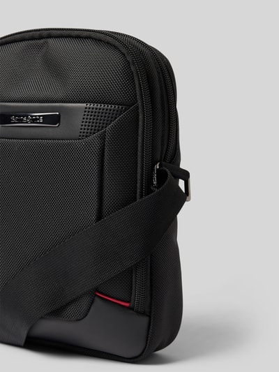 Produktfoto, schwarze Crossbody Bag mit Logo-Detail Modell 'Pro DLX' von Samsonite aus strukturiertem Material, Reißverschluss, Nahaufnahme. Geteiltes Hauptfach, verstellbarer Schulterriemen, Maße: 19x27x8 cm, Länge Schulterriemen: 90 cm.