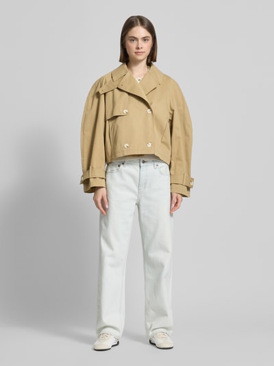 Vrouwenmodel draagt trenchcoat met mouwsluitingen model 'MIA' van Topshop, puur katoen, regular fit, platte kraag, knoopsluiting, met dubbele rij knopen, zandkleur, textuur glad, lengte tot heup, zichtbare details en naden, dames, Ganzkörperansicht von vorne.