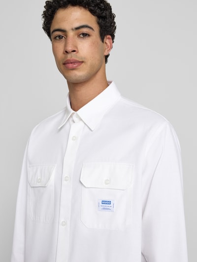 Męskimodel nosi Oversized Freizeithemd aus reiner Baumwolle Modell 'EKYNONE' od HUGO, jednokolorowy, splot twill, naszywka z logo, koszula casualowa, krój oversized, kołnierzyk typu kent, długi rękaw, sportowe mankiety, nakładane kieszenie na piersi. Nahaufnahme Oberkörper.