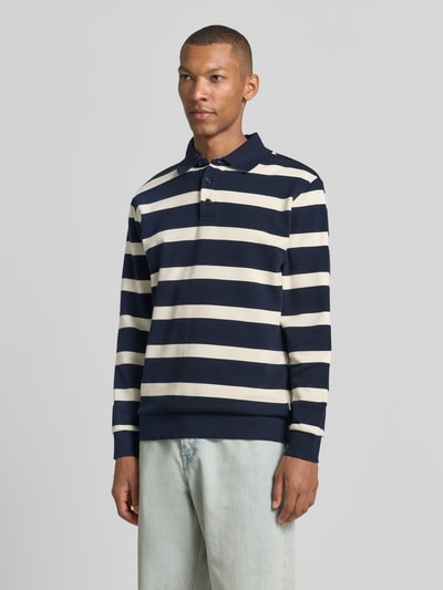 Männermodel trägt Regular Fit Poloshirt von Lindbergh in Navy und Weiß gestreift, Baumwoll-Mix, elastische Abschlüsse, Ganzkörperansicht von vorne. Rückenlänge bei Größe M: 74 cm, Polokragen mit Knopfleiste.