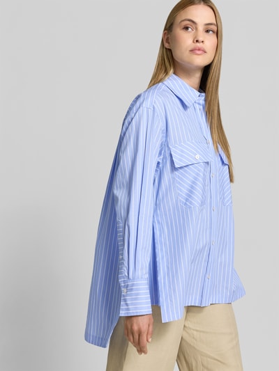 Frauenmodel trägt Relaxed Fit Hemdbluse aus Baumwolle von Joseph, hellblau mit weißen Streifen, langärmelig, verlängerte Rückseite, Ganzkörperansicht von vorne.